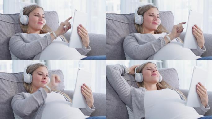 一个放松的怀孕年轻女子在家沙发上使用数字平板电脑和耳机的4k视频片段