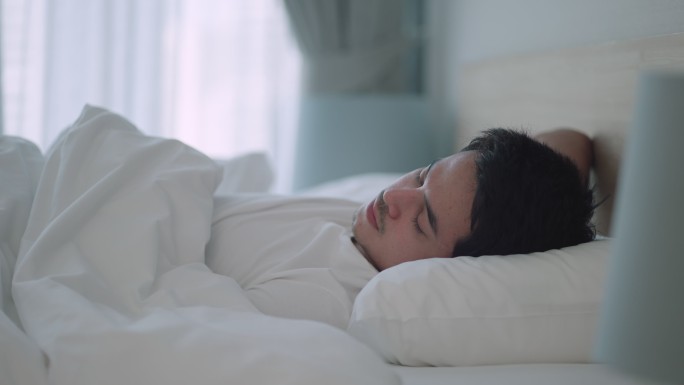 亚裔男子在家里卧室的床上舒适地小睡，做着甜美的梦