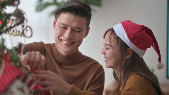 亚裔中国年轻夫妇在家里庆祝圣诞节，客厅装饰圣诞树