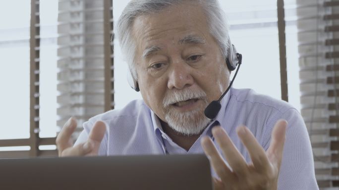 有经验的老年商人在家庭办公室使用笔记本电脑进行会议视频通话或录制网络研讨会。