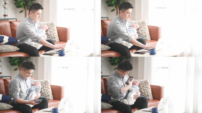 一名亚裔中国男子背着坐在沙发上的男婴在客厅里工作