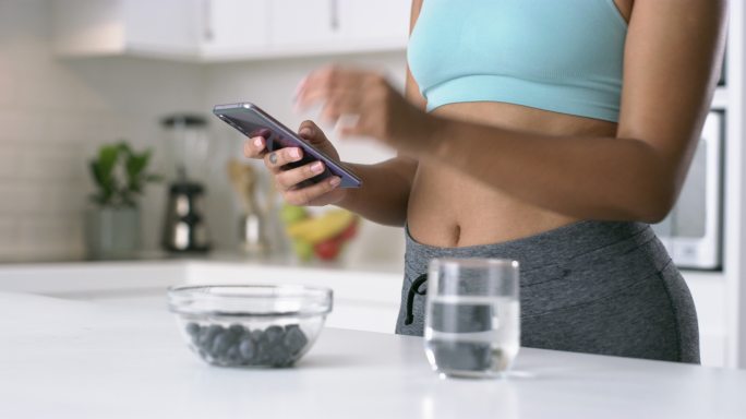 4k视频片段，一名无法辨认的女性在家锻炼后使用智能手机吃健康零食