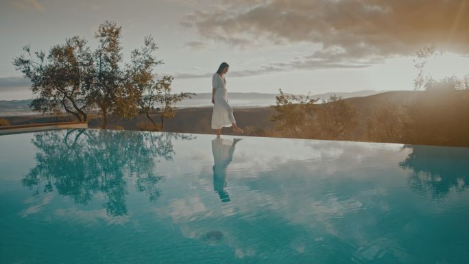 日落时分，穿着白色连衣裙的斯洛莫女士在泳池边踢水