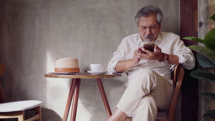 亚洲老年人坐在咖啡厅咖啡厅使用智能手机的照片，老年人输入短信和移动设备，人们生活方式技术概念