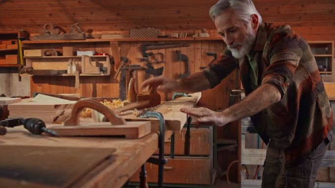 高级男木匠在他的店里用刨子把木板刨成方形