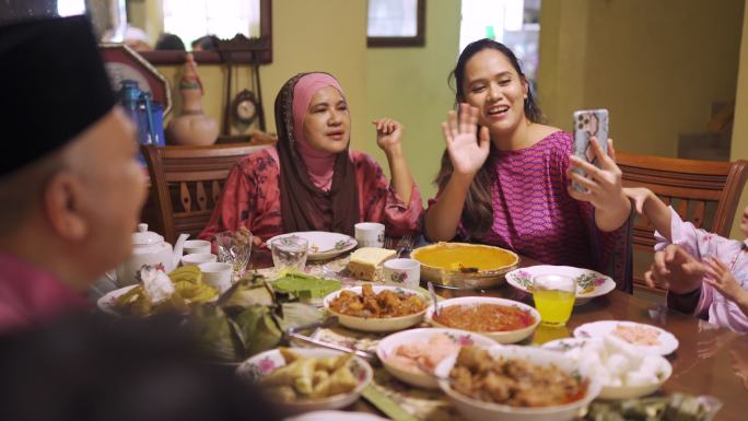 斋月哈里拉亚马来西亚穆斯林多代家庭挥舞着视频电话，亲戚在家里的餐厅享用晚餐