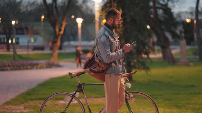 黄昏时分，现代年轻人一边用手机上网，一边推着他的复古自行车