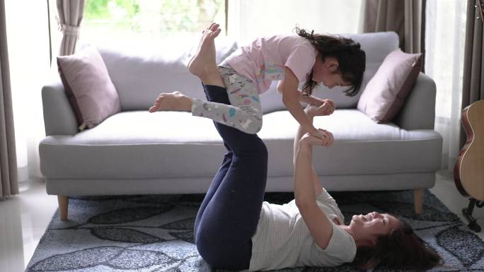 健康的妈妈和女儿在家里客厅里快乐有趣地玩平衡游戏