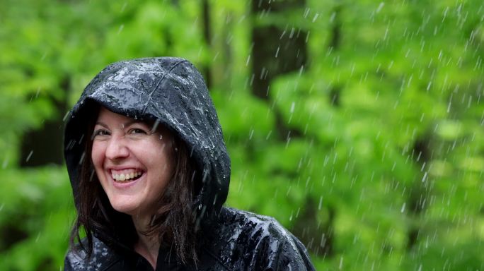 快乐的女人穿着雨衣在森林里徒步旅行