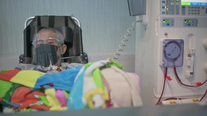 在医院接受透析治疗的亚裔中国老人，带着面罩，坐在轮椅上