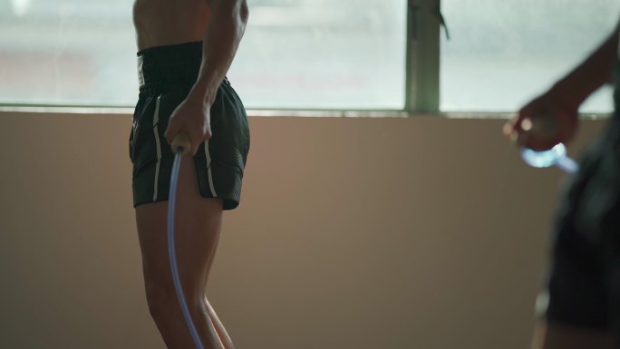 中年亚洲男运动员在健身房健身俱乐部跳绳锻炼，白天在窗户旁边放一排黄色的沙袋
