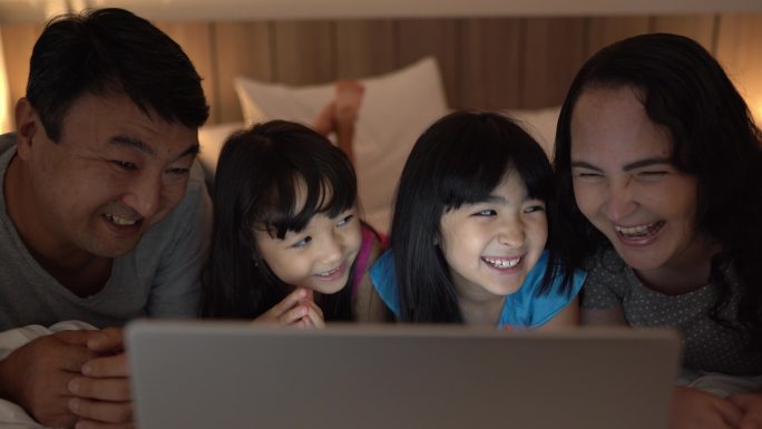 一家人在家里的床上用笔记本电脑进行视频通话
