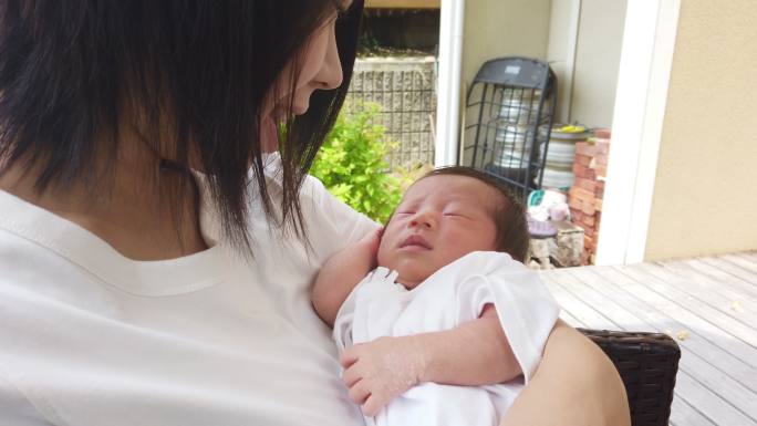 新生儿抱着母亲的手指，坐在屋外放松。