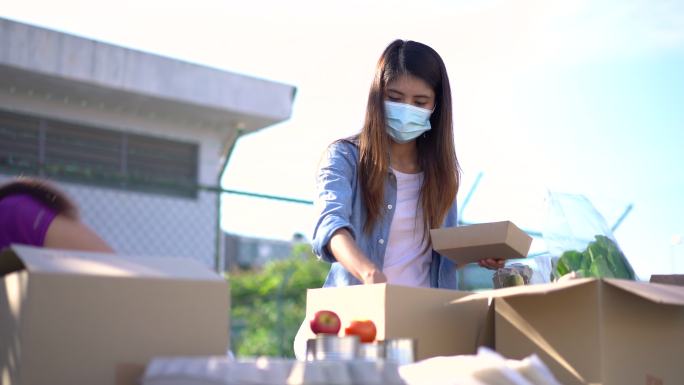 两名年轻的亚洲女性志愿者在食品银行打包捐赠物品