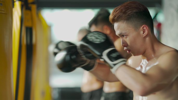 极限运动亚洲男子泰拳拳击手连续打沙袋一起在健身俱乐部练习