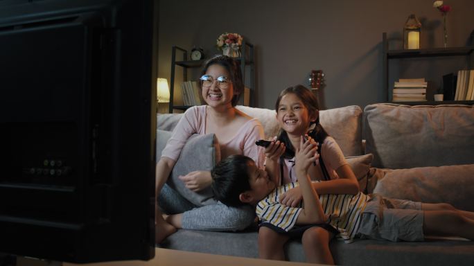 亚裔家庭的兄弟姐妹在电视上看体育节目，晚上在家里开心兴奋