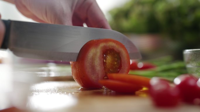 特写镜头：女性在烹饪板上用刀将新鲜的红色番茄切成薄片