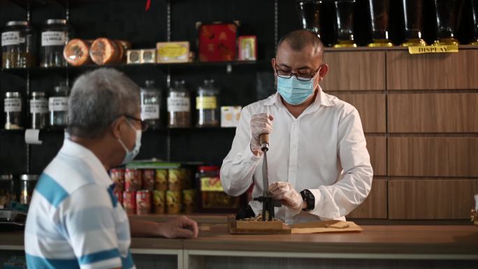 亚裔中国男药剂师在中药店为年长的病人切人参中药