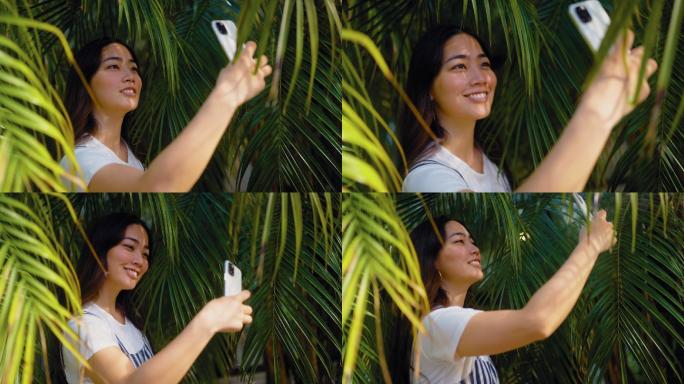 年轻女子在棕榈树叶间使用智能手机