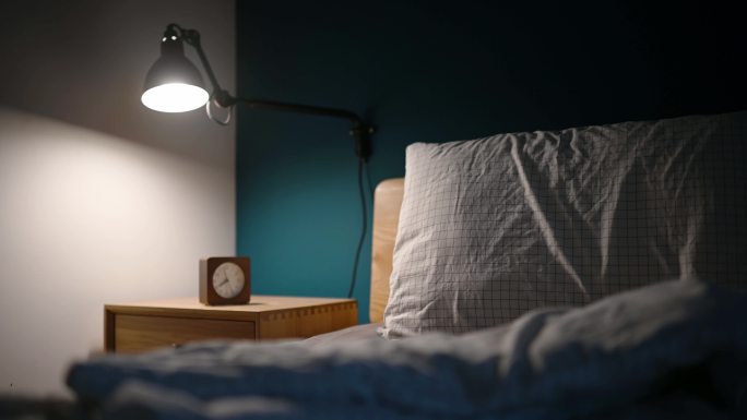 夜间卧室由电灯照明，床头柜上有时钟，床边有蓝色的墙壁