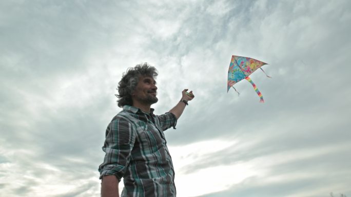成熟的男人在阴郁的天空中放风筝。童年的乐趣。低角度观看。