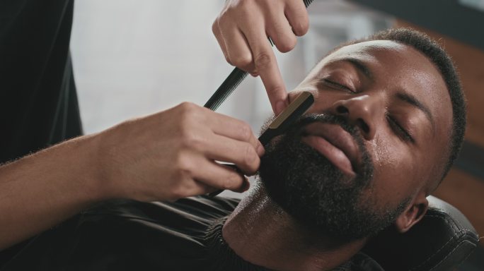 一段4k视频，一个英俊的年轻人坐在理发店，被理发师剃胡子