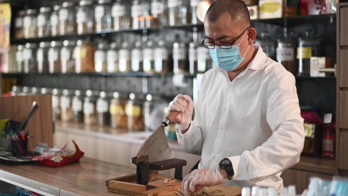 亚裔中国男药剂师在中药店切人参中药