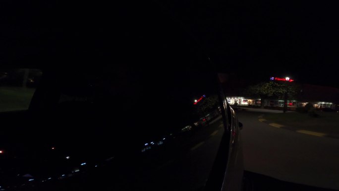 Timelapese。一名男子在夜间驾驶一辆汽车环城而行，车窗上反射着城市的灯光。