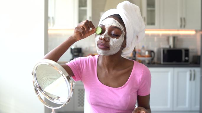 4K视频美丽的年轻非裔美国女性，脸上戴着奶油面膜，眼睛上贴着黄瓜片