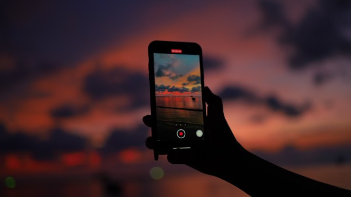 在智能手机上记录日落海滩景观的女性手