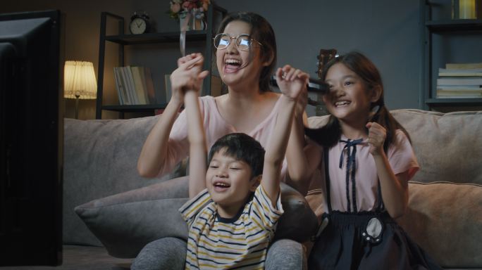 亚裔家庭的兄弟姐妹在电视上看体育节目，晚上在家里开心兴奋
