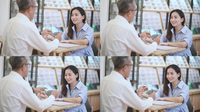 亚裔华裔工作高级男子在眼镜店向正在镜子前试镜的女性顾客解释
