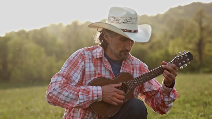 大自然中的牛仔在日落时弹吉他。春季度假。