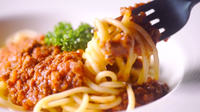 叉子的慢动作将意大利面旋转成意大利面猪肉，配上番茄酱，放在盘子里