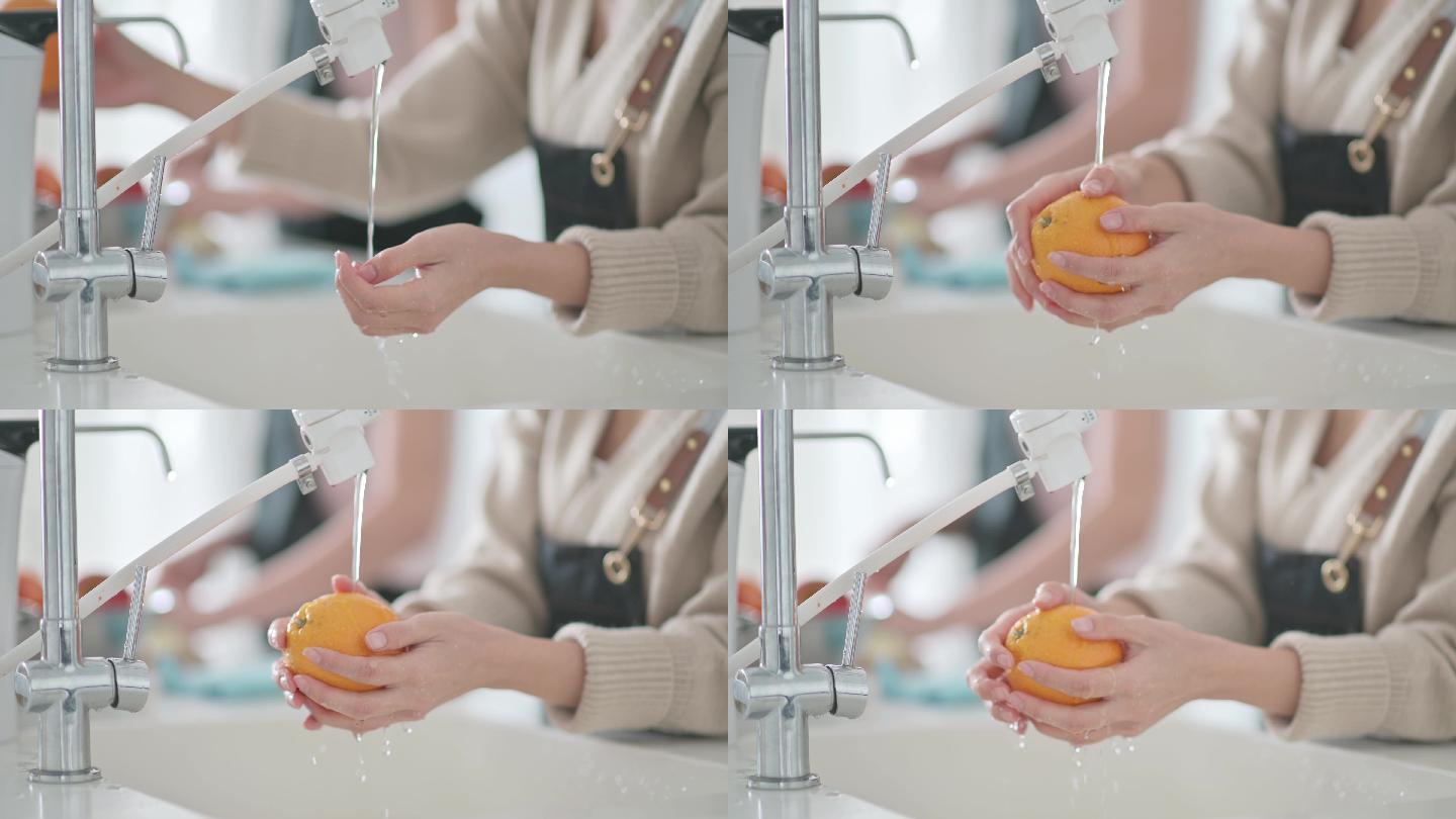 周末，亚裔中国女性在家里用笔记本电脑在厨房柜台用自来水洗手，清洗水槽里的橙色水果