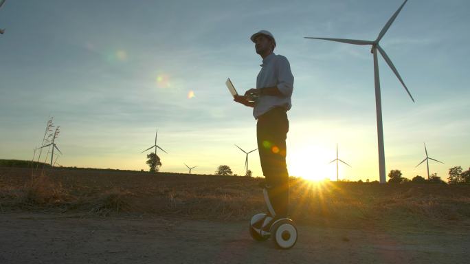 日落剪影年轻男性工程师在风力发电站工作，在风力发电场工作，使用替代电动滑板车生产能源。现代科技。另一