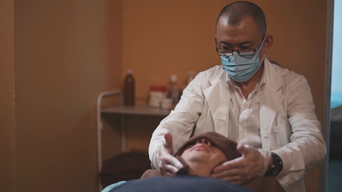 亚洲男性按摩治疗师按压患者头部穴位缓解压力指压