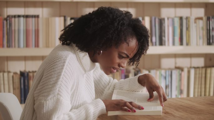 非洲裔女性在客厅里读着迷人的书。情节扭曲的情绪反应。