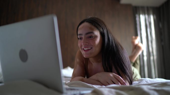 年轻女子在家里的床上看笔记本电脑上的东西