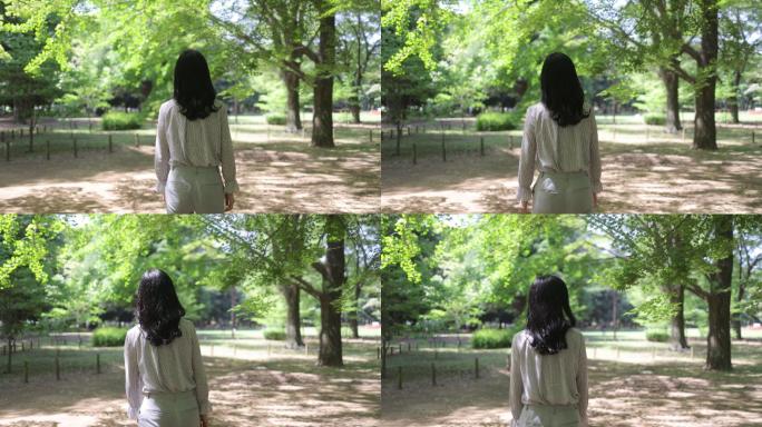 一名日本女子在公园里行走的后视图，在新鲜的绿叶下
