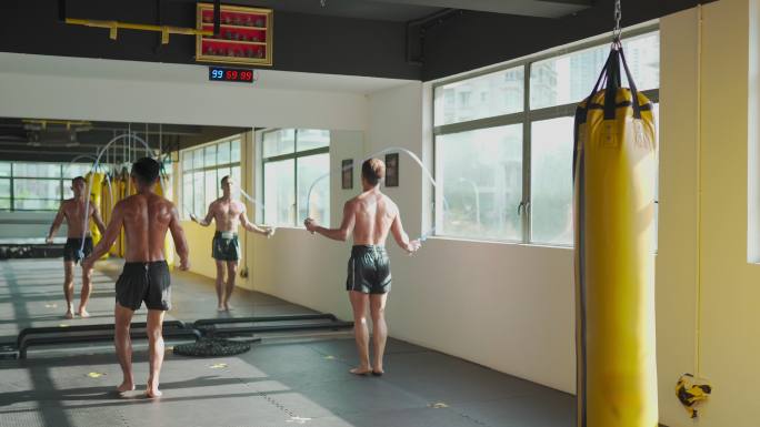 亚洲男运动员在健身房健身俱乐部跳绳锻炼，白天在窗户旁边放一排黄色的沙袋