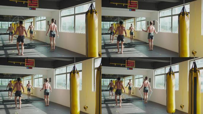 亚洲男运动员在健身房健身俱乐部跳绳锻炼，白天在窗户旁边放一排黄色的沙袋