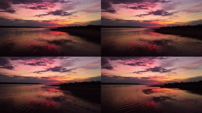 明亮的暗红色夕阳黄昏天空云朵飞过水面鸟瞰