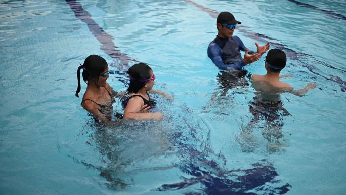 2名亚裔中国教练在游泳池里教他们的年轻学生漂浮在水面上