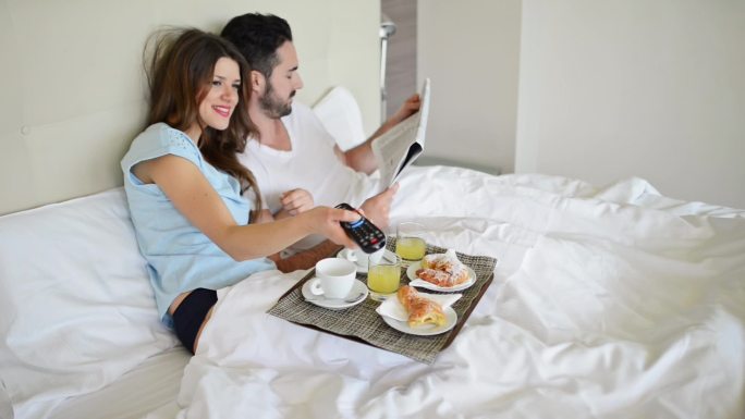 一对夫妇一边看电视一边在床上吃早餐