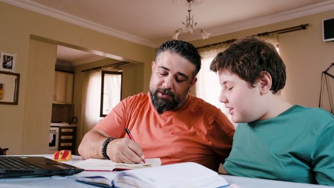 愤怒的父亲白天坐在笔记本电脑前的桌子旁，在家里帮助压力重重的十几岁的儿子做作业