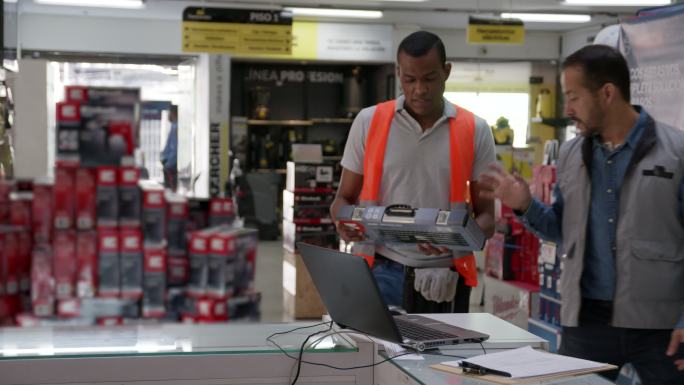 拉丁美洲的一名销售员帮助一名顾客在一家五金店购买工具箱，并检查系统的价格