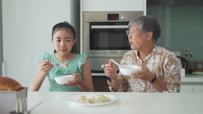 一位亚裔华裔老太太和她的孙女在厨房柜台前吃饺子