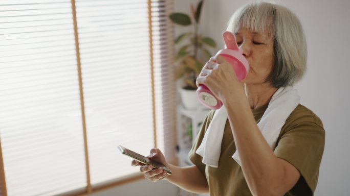 老年女性在锻炼和喝健康饮料后检查心率和卡路里燃烧状态