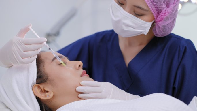 美丽的亚洲年轻女子正在美容诊所接受面部注射，使其焕发青春。专家美容师正在用A型肉毒毒素填充女性皱纹。